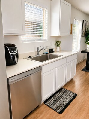 A modern kitchen with a dishwasher, stainless steel sink, and white cabinetry.