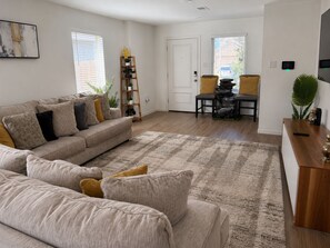 A living room with a sofa, a coffee table, and a rug. There is a door and a window with blinds.