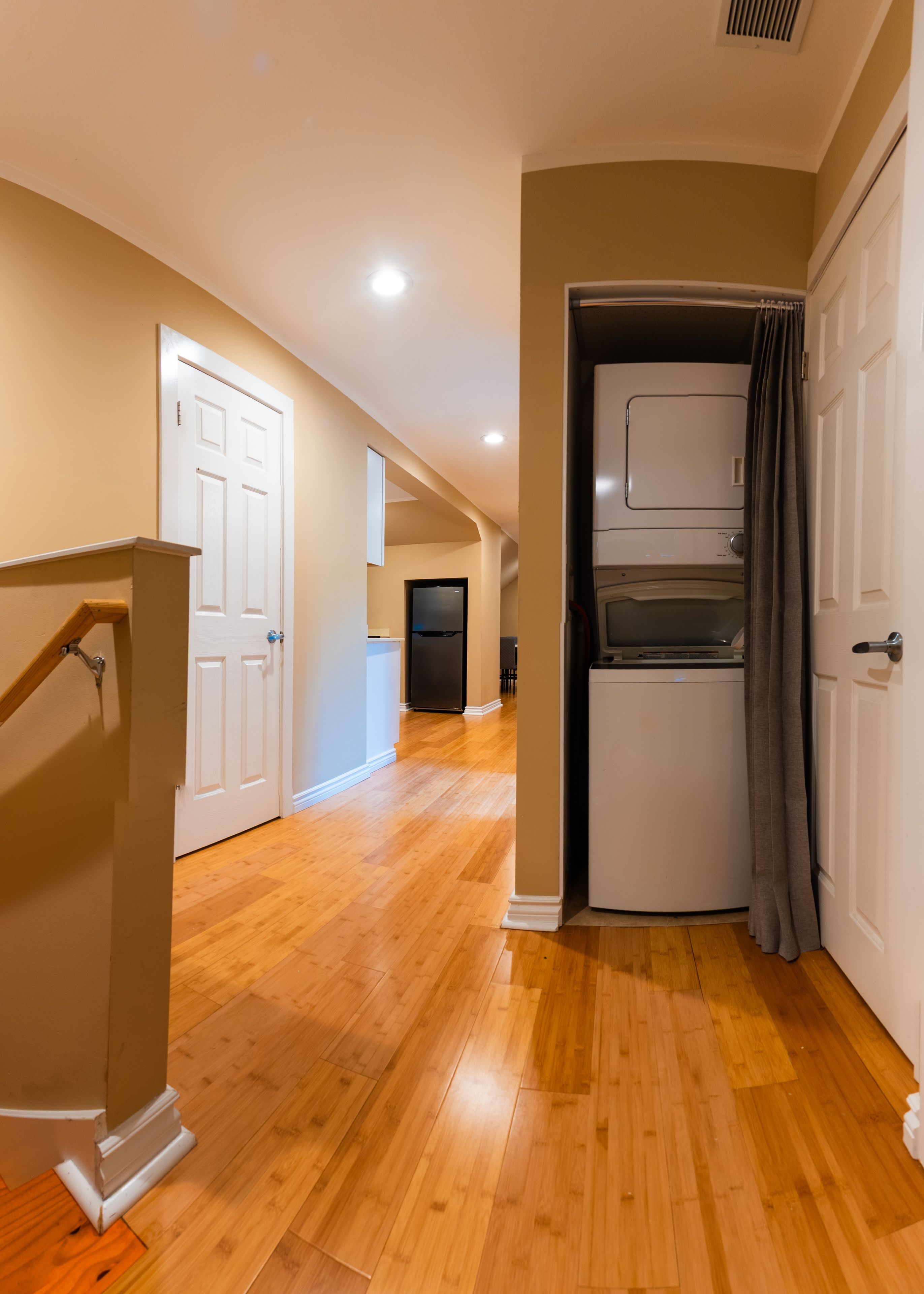 An interior hallway with wooden flooring, white doors, and a built-in washer and dryer unit.