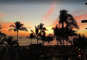 Una spiaggia con palme nere all'orizzonte su un cielo al tramonto.