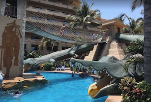 Un espace piscine doté d’un grand toboggan en forme de crocodile et d’un pont de corde.