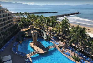 Un resort con una grande piscina, palme e vista sull'oceano.