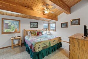 A bedroom with a large bed, a desk, and a ceiling fan. There are windows and framed pictures on the walls. - Ski-In/Ski-Out Schweitzer Chalet w/ Hot Tub (Sandpoint)