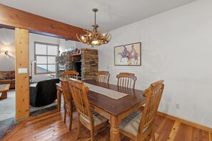 A dining area with a wooden table, chairs, a chandelier, a fireplace, and a painting on the wall. - Ski-In/Ski-Out Schweitzer Chalet w/ Hot Tub (Sandpoint)