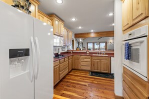 A modern kitchen with wooden cabinets, a white refrigerator, a microwave, and an oven. - Ski-In/Ski-Out Schweitzer Chalet w/ Hot Tub (Sandpoint)