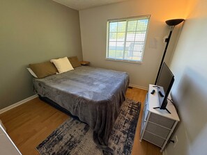 Quarto com uma cama, mesa de cabeceira, abajur e janela.