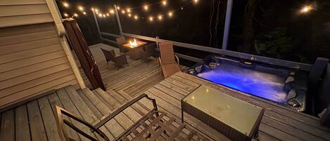 A wooden deck with outdoor furniture, a hot tub with blue lighting, and string lights.