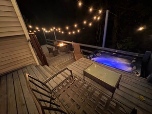 Um deck de madeira com móveis de exterior, uma banheira de hidromassagem iluminada em azul e luzes de fada.