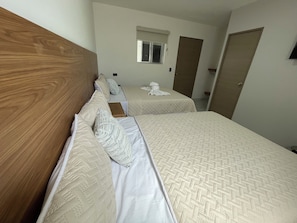 A hotel room with two beds, a wooden headboard, a window, and a door.