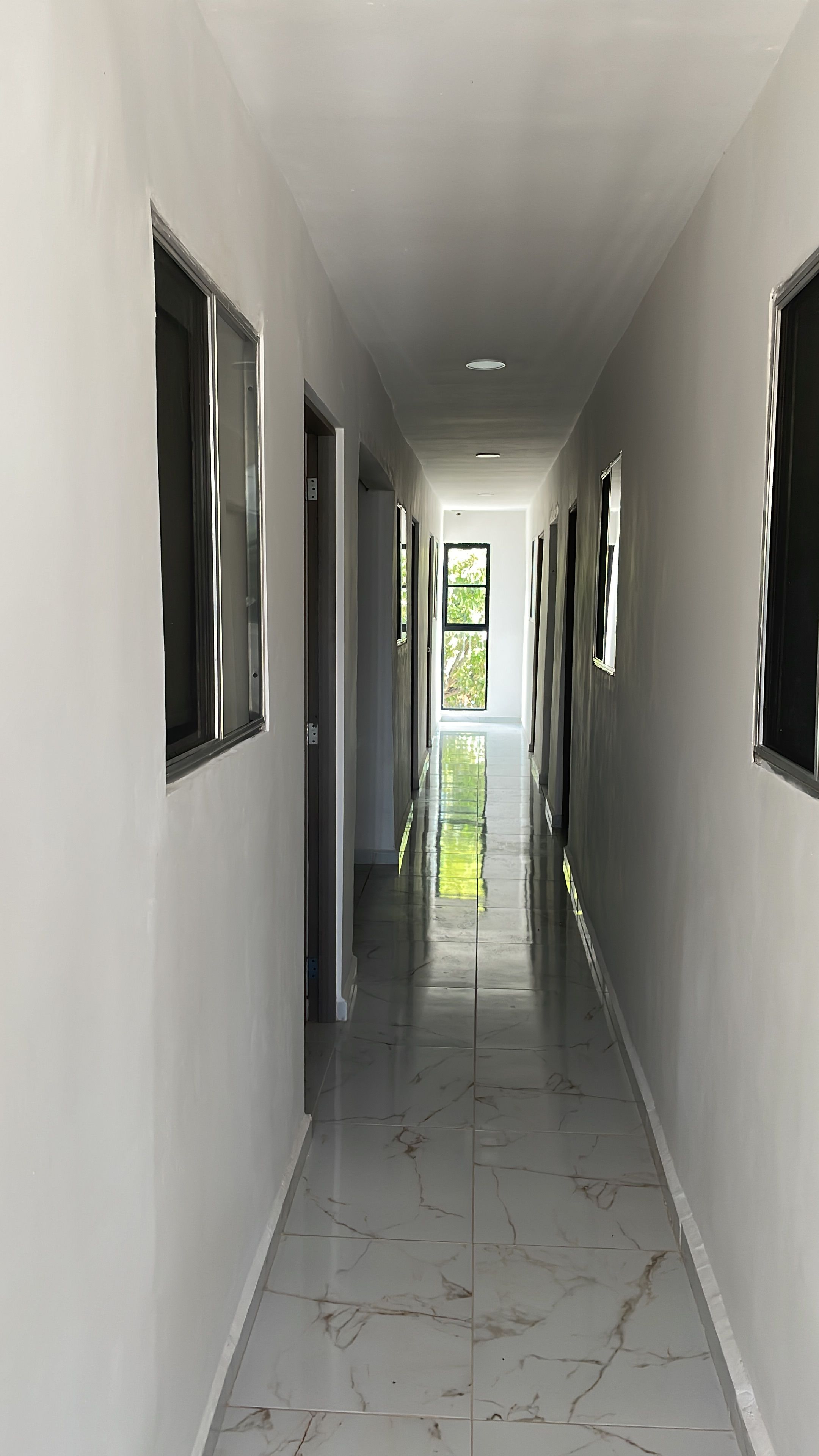 Un pasillo largo y estrecho con piso de baldosas brillantes y varias ventanas a cada lado.