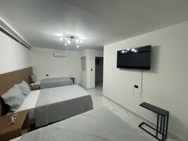 Habitación de hotel con dos camas, televisión de pantalla plana, aire acondicionado e iluminación moderna en el techo.