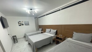Et hotelværelse med to senge, en træsengegavl, et lille natbord, et vægmonteret fjernsyn og en lampe i loftet.