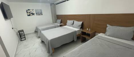 A hotel room with two beds, a wooden headboard, a small bedside table, a wall-mounted TV, and a ceiling light fixture.