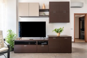 Ein modernes Wohnzimmer mit Flachbildfernseher, dunklem Holzunterhaltungsschrank und einer Topfpflanze.