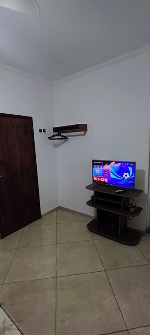 Un salon avec un téléviseur à écran plat posé sur un meuble, une porte en bois et un mur blanc.