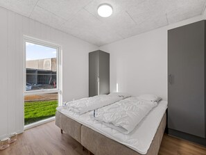 A bedroom with a bed, a wardrobe, and a window with a view of a building and greenery. - "Fita" - 450m from the sea by Interhome (Ringkøbing)