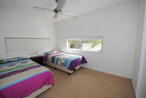 A bedroom with two beds, a ceiling fan, a window, and a nightstand with a lamp.
