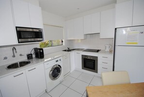 Une cuisine moderne avec des meubles blancs, un four à micro-ondes encastré, une machine à café, un lave-linge et un réfrigérateur.