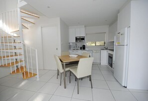 A modern kitchen with white cabinetry, a dining table with chairs, and a staircase with wooden steps.