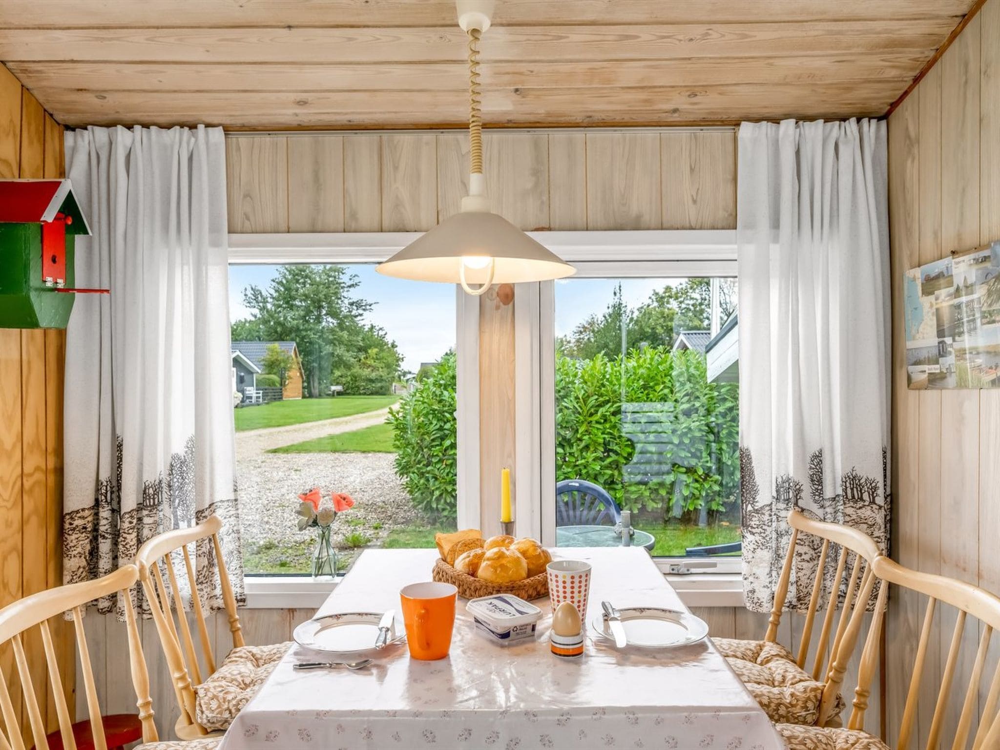 A dining area with a table set for two, a window with curtains, and a view of the outdoors.