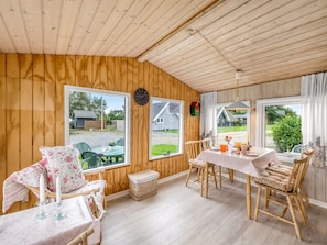 A cozy room with wooden walls and ceiling, large windows, a dining table with chairs, and a small table with a chair. - "Kierulf" - 1km to the fjord by Interhome (Hemmet)