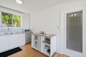 A modern kitchen with white cabinetry, a microwave, and a built-in shelf unit with dishes. - Sandy Bay Retreat with Marina Views – 2 Bedroom (Sandy Bay)