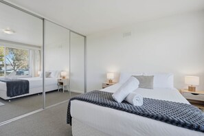 A modern hotel room with a large bed, bedside tables, a mirror, and a view of the outdoors. - Sandy Bay Retreat with Marina Views – 2 Bedroom (Sandy Bay)