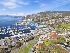 A marina with multiple boats docked, surrounded by residential buildings and a hilly landscape in the background. - Sandy Bay Retreat with Marina Views – 2 Bedroom (Sandy Bay)