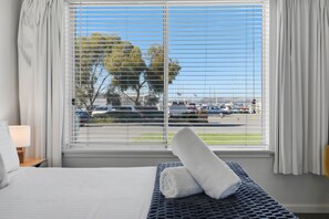 Een hotelkamer met een bed, een raam met zonwering, uitzicht op een jachthaven en een handdoek op het bed.