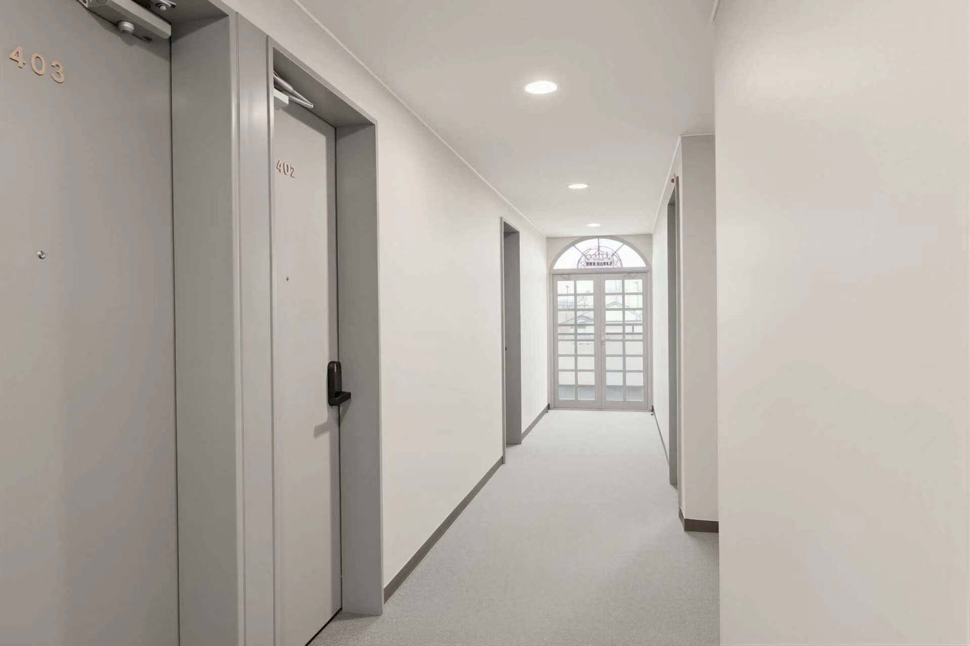 Un couloir avec les portes numérotées 402 et 403, qui donnent sur une pièce dotée d’une grande fenêtre.