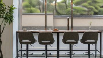 A modern interior with a wooden table and four grey chairs, a potted plant, and a view of greenery outside.