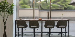 Un interior moderno con una mesa de madera y cuatro sillas grises, una planta en maceta y vistas al exterior con vegetación.