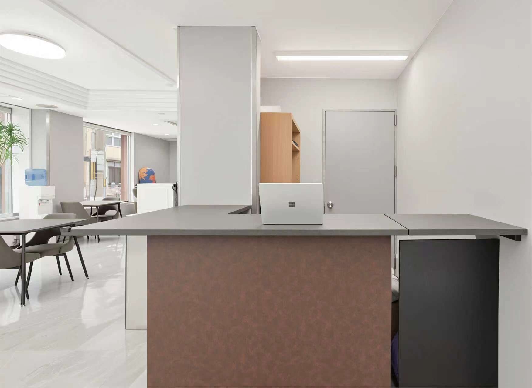 Un espace de bureau moderne avec un comptoir d’accueil, un ordinateur portable et une porte en arrière-plan.