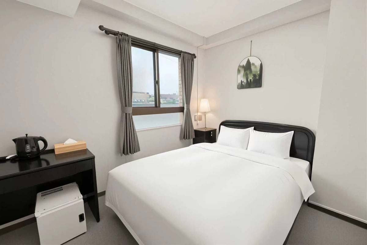 Une chambre d’hôtel équipée d’un lit, d’un bureau, d’une bouilloire, d’une lampe et offrant une vue sur la ville.