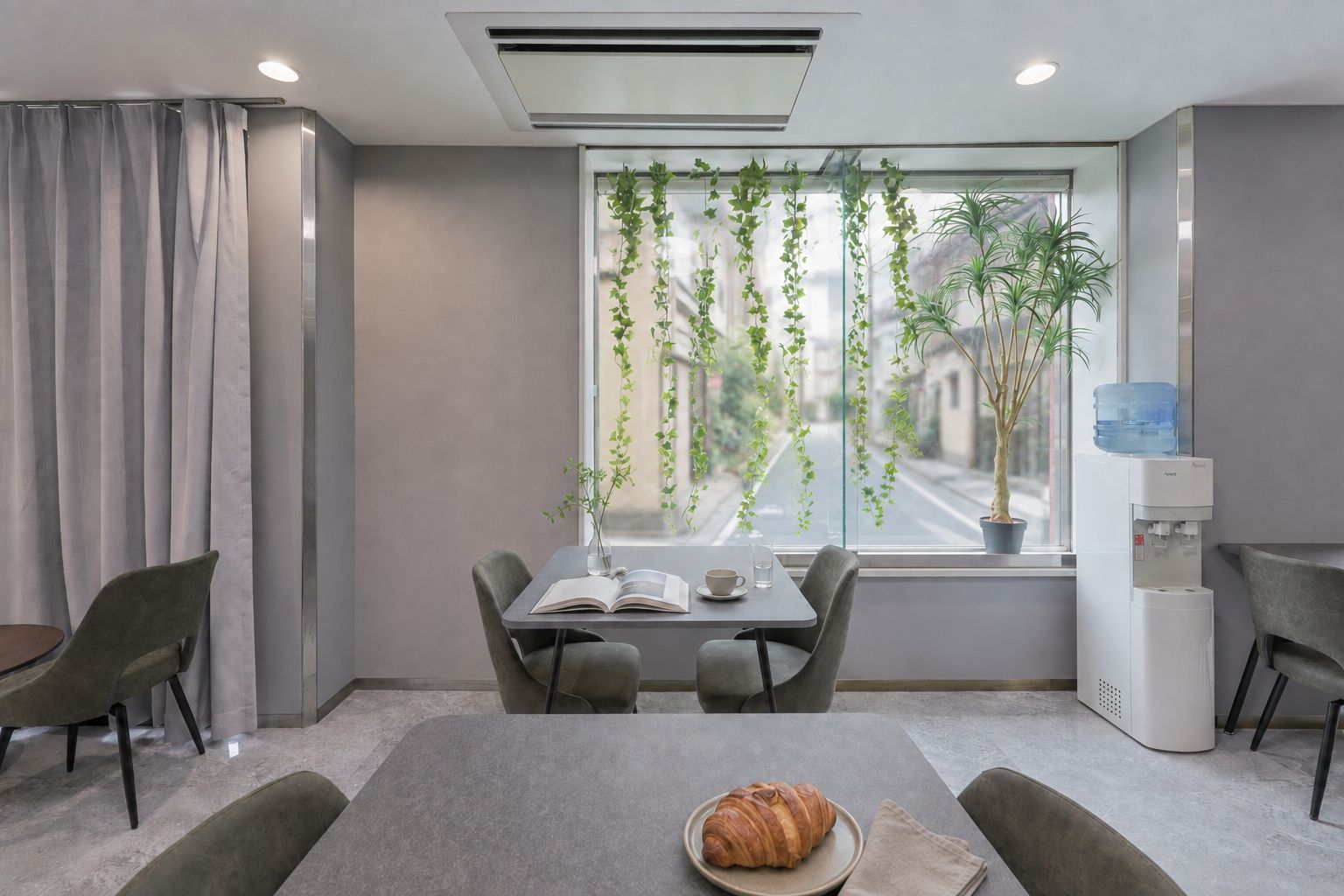 Une pièce moderne équipée d’une table à manger, de chaises, d’un distributeur d’eau et d’une fenêtre agrémentée de plantes.