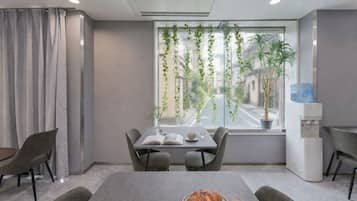 A modern room with a dining table, chairs, a water dispenser, and a window with plants.