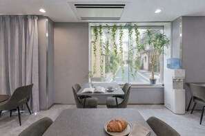 Una habitación moderna con una mesa de comedor, sillas, dispensador de agua y una ventana con plantas.