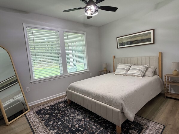 A bedroom with a bed, a ceiling fan, a window with blinds, a bedside table with a lamp, and a rug. - Cozy and fun modern cottage in Luray, VA. (Luray)
