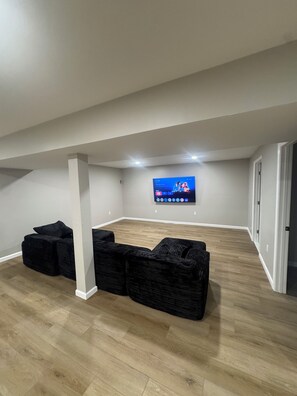 A room with a flat-screen TV mounted on the wall, a wooden floor, and a black sectional sofa. - Cozy and fun modern cottage in Luray, VA. (Luray)