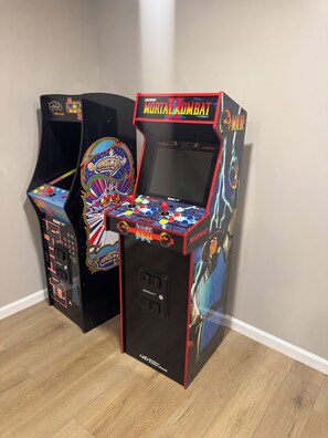 Two arcade machines, one labeled 'Midway' and the other 'Mortal Kombat,' placed against a plain wall. - Cozy and fun modern cottage in Luray, VA. (Luray)