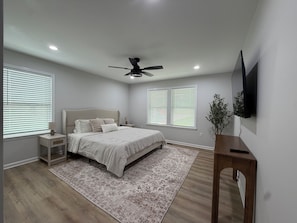 A bedroom with a bed, nightstands, a ceiling fan, a TV, and a large window with blinds. - Cozy and fun modern cottage in Luray, VA. (Luray)