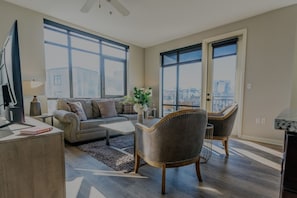A modern living room with a sofa, coffee table, and two armchairs. There is a large window providing a view of the cityscape. - Luxurious 2 bed 2 bath Corner Unit-City View #521 (Nashville)