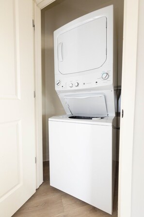 A compact, white front-loading washer and dryer unit in a narrow hallway with a wooden floor. - Luxurious 2 bed 2 bath Corner Unit-City View #521 (Nashville)