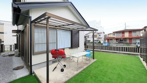 Ein Wohngebäude mit überdachter Terrasse, Grill und kleinem Tisch.