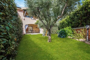 A well-maintained garden with a lawn, a tree, and a building with a balcony. - Casa Angela With Pool, Pittulongu, Italy (Pittulongu)