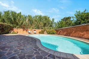 A swimming pool with a stone deck, surrounded by a brick wall and lush greenery. - Casa Angela With Pool, Pittulongu, Italy (Pittulongu)