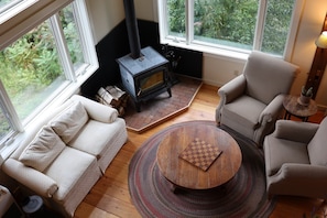 A cozy living room with a sofa, armchair, and a round coffee table. A fireplace with a chimney is visible in the corner.