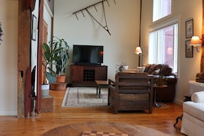 Una sala de estar con televisión, muebles de madera, un sofá y una ventana.