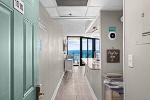 A hallway with a view of the ocean, a door labeled '1010', a sign indicating a 'flop drop', and a '24-hour' service sign. - Gulf-Front Condo | Beach Chairs, Balcony & 3 Pools (Panama City Beach)