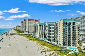 A beachfront hotel with multiple high-rise buildings, a sandy beach, and a clear blue sky. - Gulf-Front Condo | Beach Chairs, Balcony & 3 Pools (Panama City Beach)